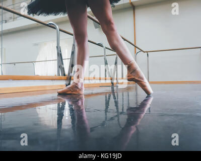 Ballerina in ballet pointe stretches on barre in gym. Woman practicing in dance studio. Work out of young girl. Stock Photo