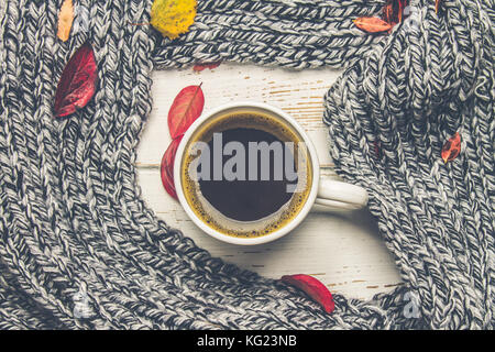 Mug of hot coffee in autumn setting on a wooden table with a knitted scarf, sweater. Comfort, warmth, cozy. Stock Photo