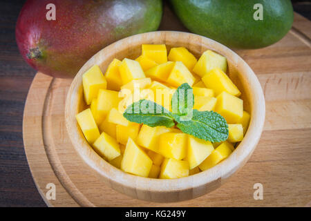 Tropical fruit mango in a plate on a wooden background, whole or sliced Stock Photo