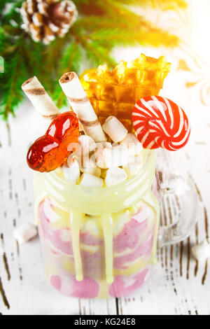 Freakshake from pink smoothie, cream. Monstershake with lollipops, waffles and marshmallow. Extreme milkshake in a Mason jar. White wooden table. Atmo Stock Photo