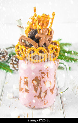 Freakshake from pink smoothie, cream. Monstershake with a chocolate man, cane, pretzels, biscuits, waffles and marshmallow. Extreme milkshake in a Mas Stock Photo