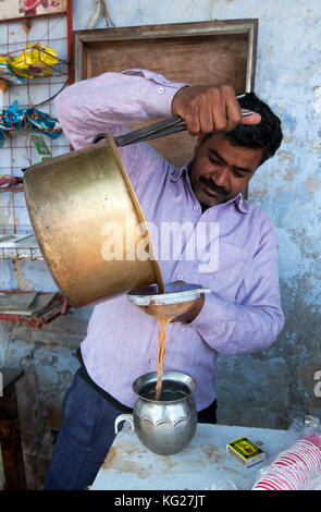 Chai wallah pouring chai from brass pan, using tongs, through sieve into tin vessel, in Diggi village market, Diggi, Rajasthan, India, Asia Stock Photo