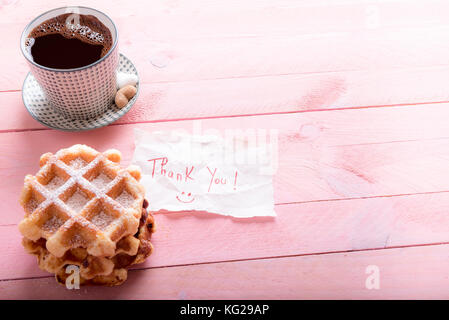 Delicious homemade waffles with a cup of hot coffee and heart shaped sugar, on a pink wooden table, and a piece of paper with the message thank you wr Stock Photo