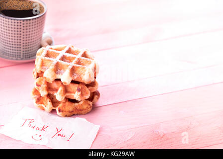 Savory snack with freshly baked waffles covered with powdered sugar, a mug of coffee and a scribble with thank you and a smiley face, on a pink backgr Stock Photo