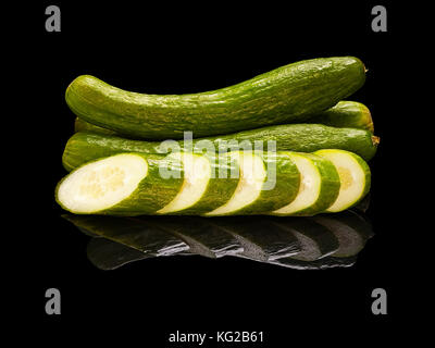 Whole long cucumbers with slices closeup isolated on black glossy background with real reflection. Side view Stock Photo