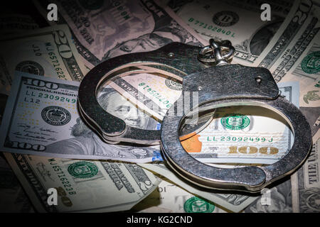 A pair of closed handcuffs on a pile of American Dollars with a deep depth of field Stock Photo