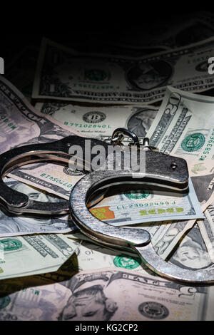 A pair of open handcuffs on a pile of American Dollars with a deep depth of field. Stock Photo
