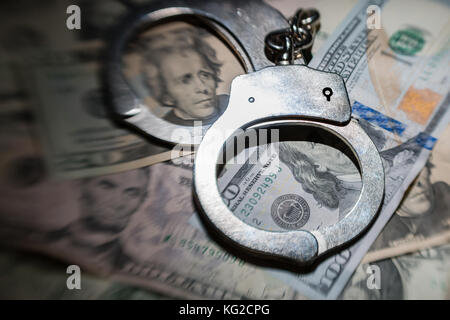 A highly selective focused shot of a pair of closed handcuffs on a pile of American Dollars Stock Photo