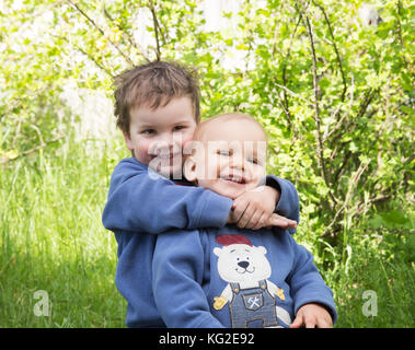 Two happy little brothers playing outdoors in the summer. The elder brother hugging young Stock Photo