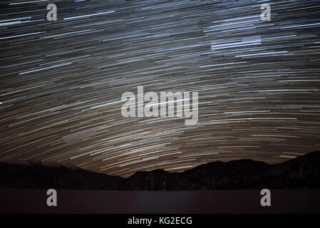 Beautiful night view with traces of stars in the form of tracks in the night sky on the background mountains with snow and sea with ice, shot with a l Stock Photo