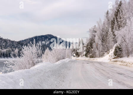 Scenic winter view from the asphalt road, covered with snow and beautiful trees in the frost on the side of the road on a background of mountains, blu Stock Photo