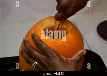 Black woman scooping seeds out of large pumpkin in preparation to carve it for Halloween festivities Stock Photo