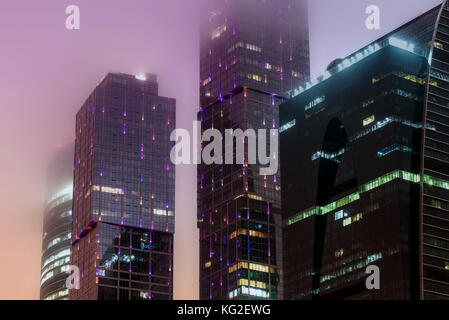 Abstract hi-tech background of fragment modern elevation office buildings of steel and glass with lights switched at night in the fog Stock Photo