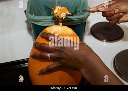 Black woman scooping seeds out of large pumpkin in preparation to carve it for Halloween festivities Stock Photo