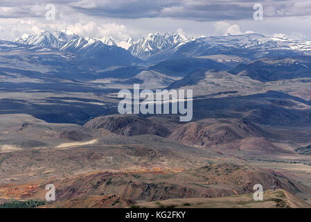 Scenic top view of the mountains covered with snow, hills and valley between the mountains on the background of cloudy sky with haze and clouds Stock Photo