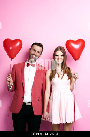 Couple hugging and holding red balloons in shape of heart on ice rink ...