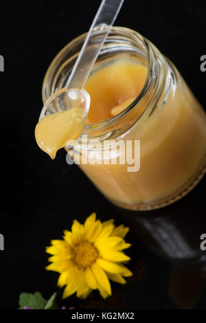 Raw organic royal jelly in a small bottle with litte spoon on small bottle on black background, France Stock Photo