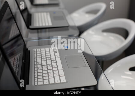 New, open laptops, on a glass desktop; modern white chairs in background. Stock Photo