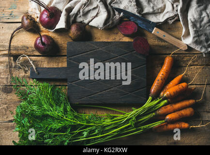 Garden carrots and beetroots with dark cutting board in center Stock Photo