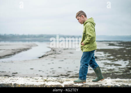 Thursday  02 November 2017 A young 8,9,10 year old boy walks along a wall wearing green wellington boots Stock Photo