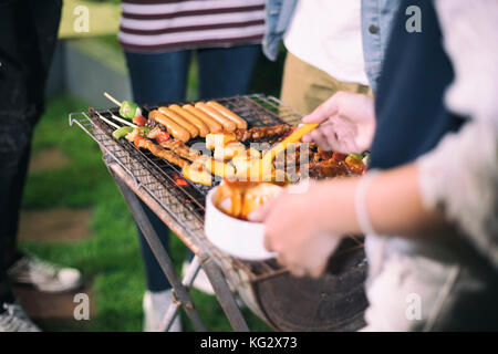 Asian group of Friends making barbecue and grilled shashliks on grate party in outdoor garden Stock Photo