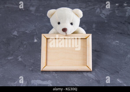 White teddy bear holding empty wooden frame. Gray background Stock Photo