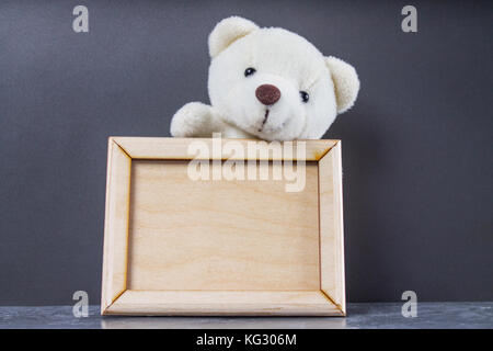 White teddy bear holding empty wooden frame. Gray background Stock Photo