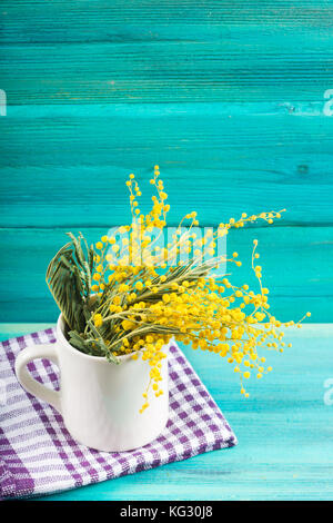 Yellow spring flowers of mimosa in a white mug on a blue wooden background Stock Photo