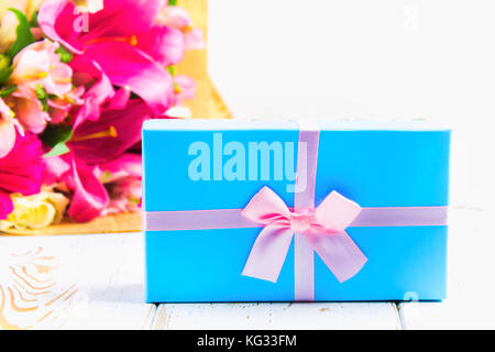 Gift in a box and a bouquet of flowers on a white wooden table. Birthday party. Stock Photo
