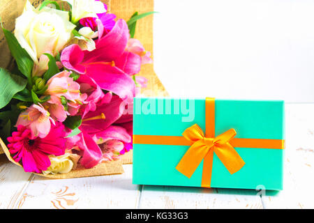 Gift in a box and a bouquet of flowers on a white wooden table. Birthday party. Stock Photo