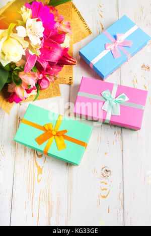 Gift in a box and a bouquet of flowers on a white wooden table. Birthday party. Stock Photo