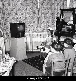 1950s, England, TV room in a children's hospital, group of small children sitting together watching a television, with one young girl held by a nurse. Stock Photo