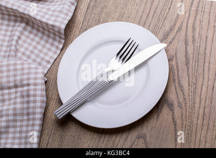 Empty plate, knife, fork and towel over wooden table background. Stock Photo