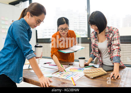 young beautiful female design team worker discussing new product plan and looking at palette paper document choosing main color during meeting. Stock Photo