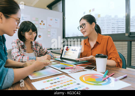 smiling pretty woman manager using mobile digital tablet pad showing design planning for her designer colleagues during company meeting. Stock Photo