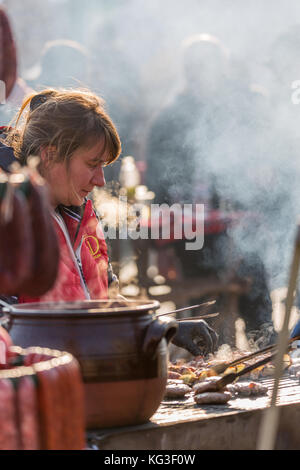 PERNIK, BULGARIA - JANUARY 27, 2017: Female cook in red apron is preparing carefully barbecue at town square at Surva, the International Festival of t Stock Photo