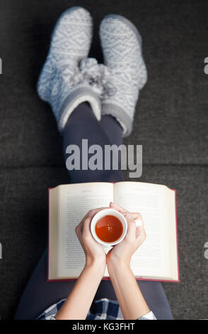 Close-up of female hands holding teacup in front of opened book Stock Photo