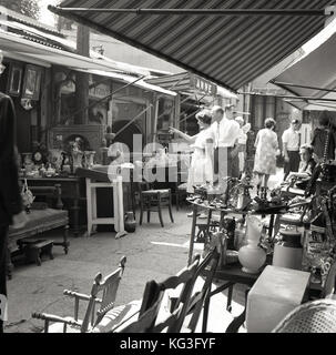 1950s, historical picture, people browsing at a stall in one of Paris's famous 'marche aux puces', flea markets, where antiques, furniture, paintings, trinkets and everything else is on sale. Stock Photo