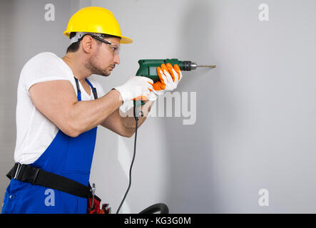 Young man using power drill on wall at home Stock Photo