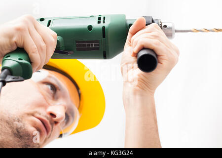 Man with helmet using electric drill making hole in wall Stock Photo