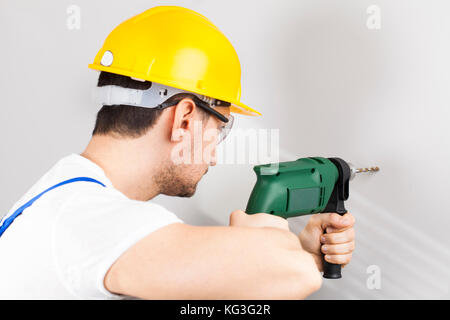Young man using power drill on wall at home Stock Photo