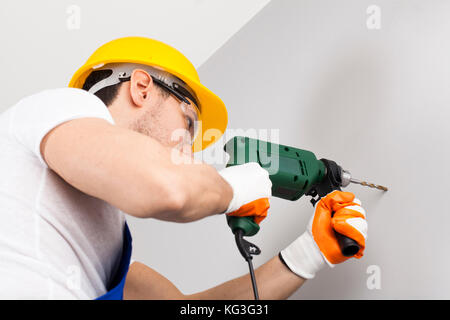 Young man using power drill on wall at home Stock Photo
