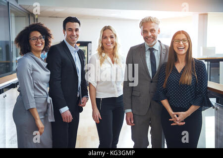 Portrait of a diverse group of confident business colleagues smiling and standing together in the hallway of a modern office Stock Photo