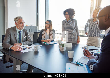 Mature manager talking to a diverse group of employees during a meeting around a table in a boardroom Stock Photo