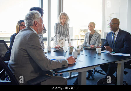 Mature manager talking to a diverse team of employees during a meeting around a table in a modern boardroom Stock Photo