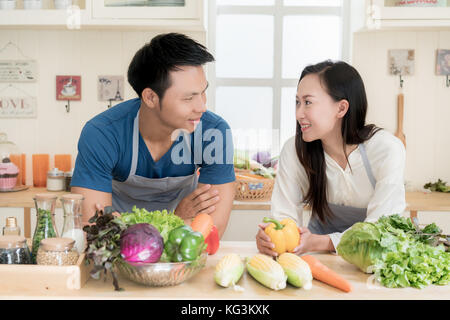Young Asian couple preparing food together at counter in kitchen. Happy love couple concept. Stock Photo