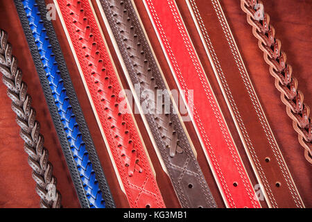 A close-up of narrow belts made of genuine red, blue and brown leather. Pattern made of leather belts Stock Photo