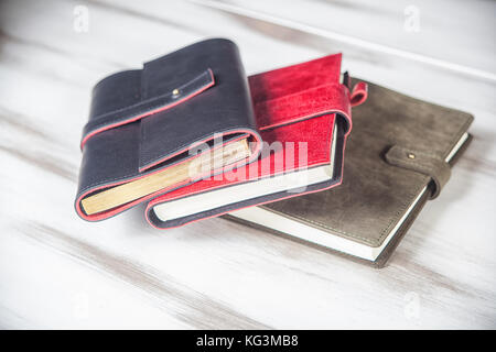 A close-up of three diaries, covered with genuine leather with a clasp: gray, red and black. Leather hand-made notebooks on a white table Stock Photo