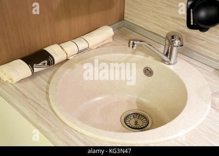 Close-up of a beige sink under a stone with a modern mettalic mixer in a beige pitcher, next to lay a kitchen of clean light towels Stock Photo