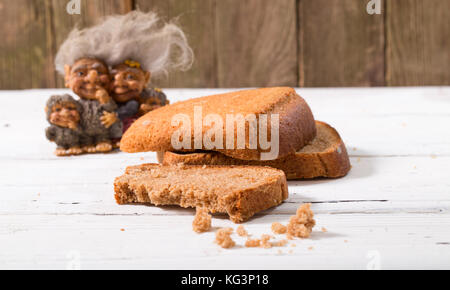 The group of fantastic beings, brownie, looks at a piece of bread. Against old gray boards, bread a rye, close up, small depth of sharpness Stock Photo